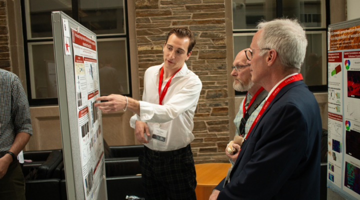 Thomas Ugras pointing to his research poster at the 2023 CHESS USER event